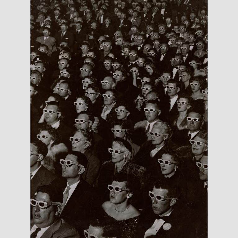A theater full of audience members wearing 3-D glasses and watching a movie. 